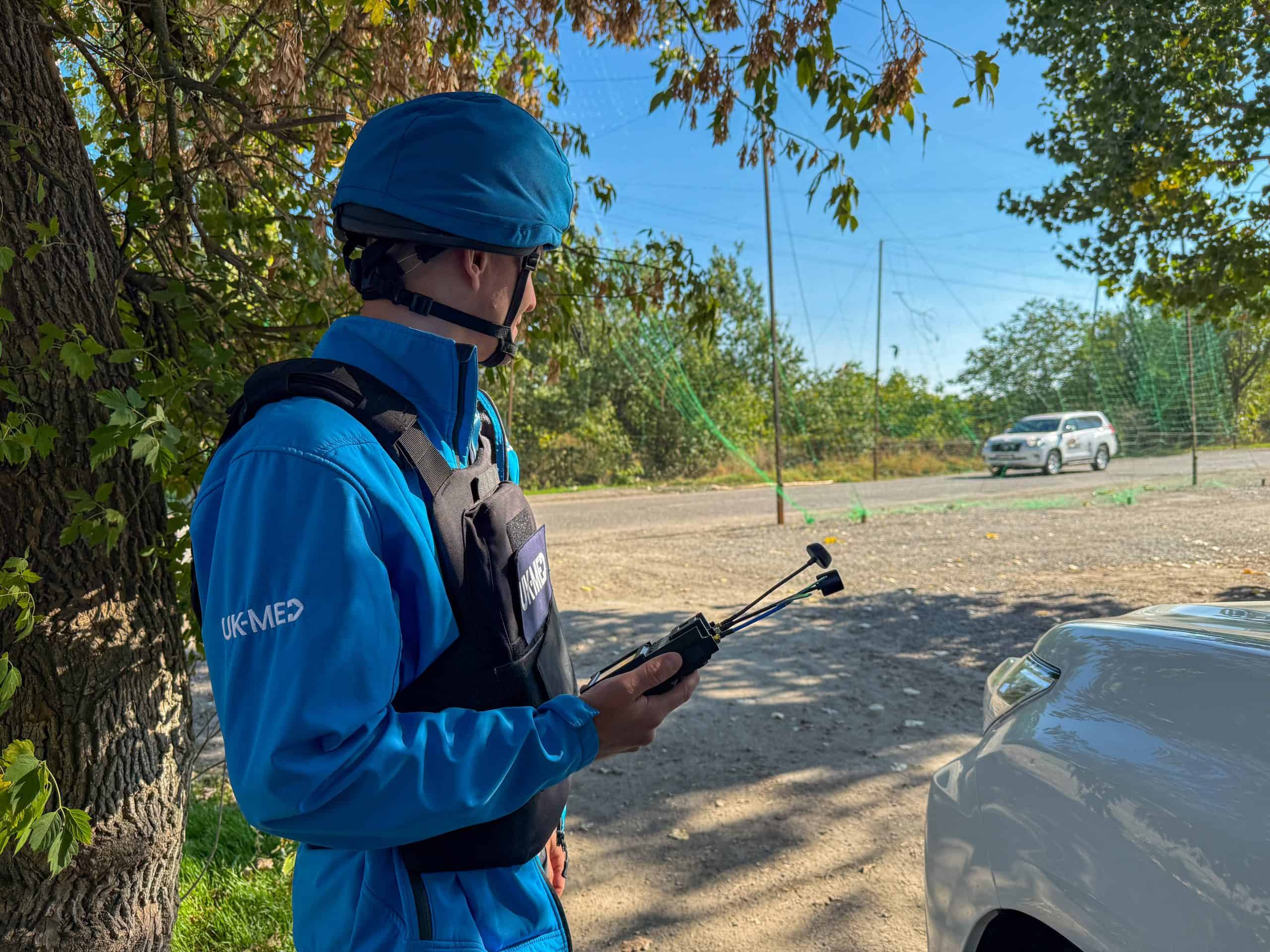 14a7a1a7-a887-4a06-9a76-1907359fd893 UK-Med staff take cover under a tree andwhilst waiting for a drone to pass overhead. Staff are equipped with a device that allows them to see what the drone pilot can see, to assess the threat.